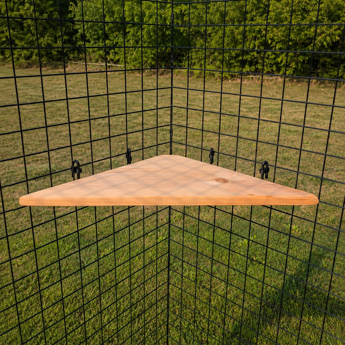 A Catio Corner Shelf is mounted on a black metal grid frame outdoors, with green grass and trees in the background.